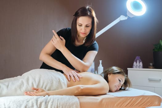 Mature woman lying on massage table and receiving medical back massage, care and treatment of middle-aged people