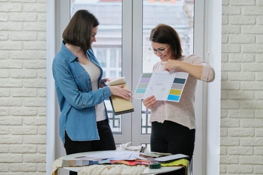 Two women choosing fabrics for curtains. Females textile designer, decorator and client watch palettes with fabrics, choose model and fabric