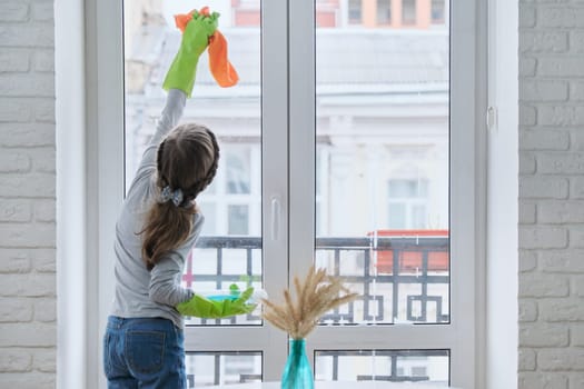 Girl child in gloves with spray detergent with rag cleaning house, washing windows, springtime, copy space