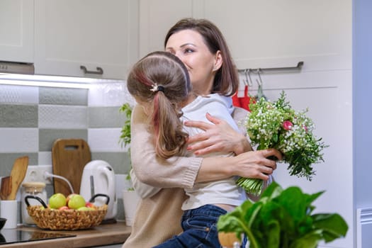 Happy mother and daughter child with spring bouquet, flowers gift of girl to her mom on mothers day. Background home kitchen interior