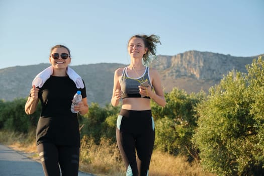 Two running women. Mother and daughter teenager running outdoor on road in mountains on summer sunny day. Family, healthy active sport lifestyle.