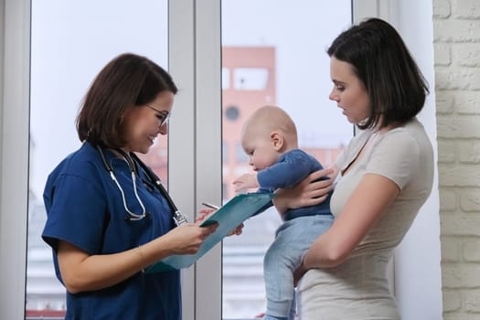 Doctor pediatrician talking with young mother holding her baby in her arms. Children medical care, health, help