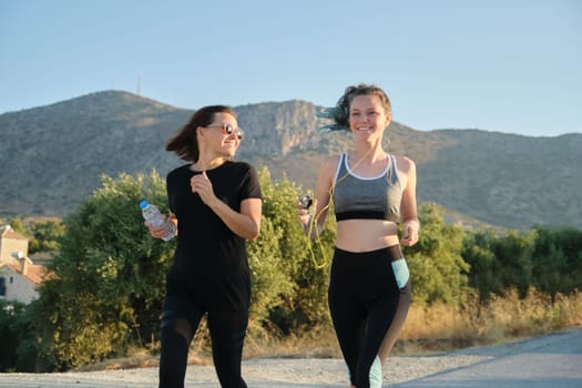 Active sports family parent and child teenager running outdoor. Mother and daughter run along mountain road