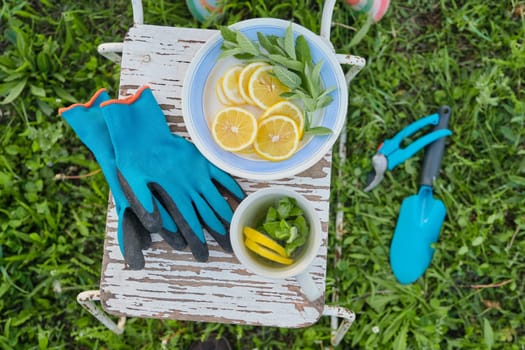 Concept of gardening, leisure, hobby. Vintage chair, secateurs, tools, gloves, cup of fresh herbal tea with mint and lemon