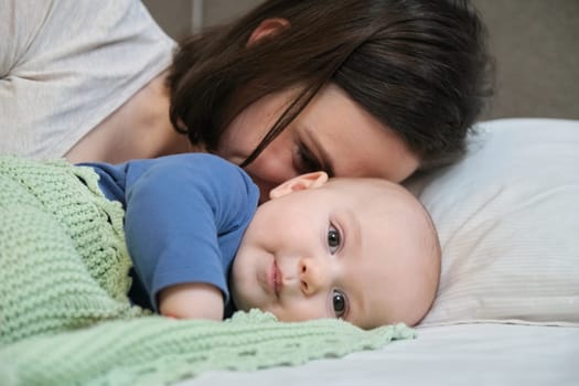 Portrait of beautiful young mother and her baby 7 month old son, parent and baby lying in bed together