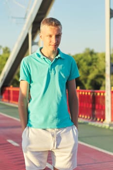 Outdoor portrait of young blond male, serious confident teenager, background blue sky, sunny summer day