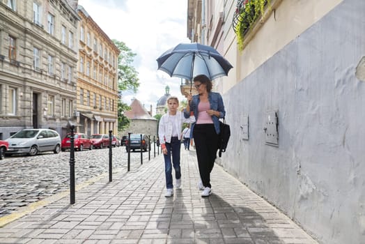 Rainy autumn weather in city, mother and daughter walking under an umbrella along street