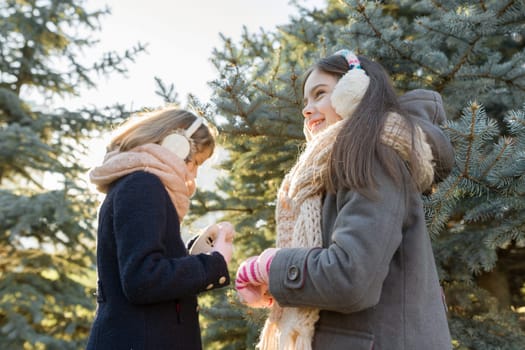 Outdoor winter portrait of two little girls smiling and having fun near the Christmas tree, golden hour