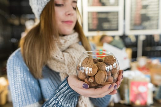 Winter portrait of young beautiful woman with bowl of hazelnuts and walnuts. Girl near bar counter in coffee shop