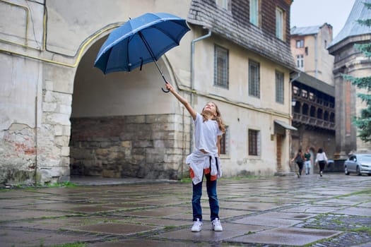 Little girl child in the rain with an umbrella, tourist old city background.