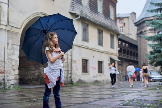 Little girl child in the rain with an umbrella, tourist old city background, copy space