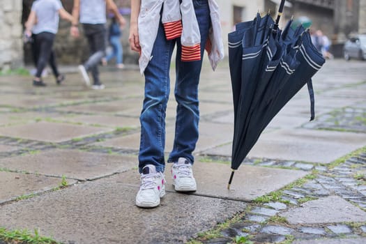 Rainy weather, legs of girl with an umbrella on wet paving stones after rain close-up