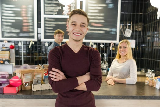 Young team of three cafe workers, people posing and smiling at coffee bar near bar counter. Teamwork, staff, small business, people concept.