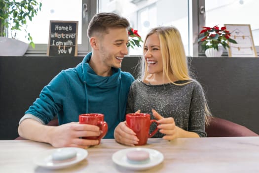 Young happy couple in love in cafe, man and woman together smile hugging, drinking coffee tea eating macaroons