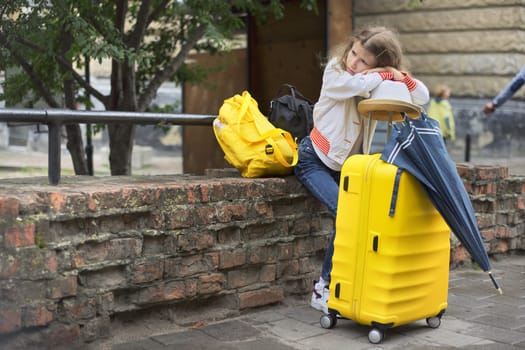 Concept of tourism, travel, little girl with luggage suitcase, backpack, hat, umbrella, close-up in tourist city