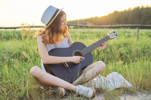 Teenager girl in hat playing the guitar, nature background, rustic style golden hour