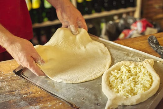 Close-up hands of male baker preparing traditional Georgian cuisine khachapuri. Process of cooking, culinary, recipe