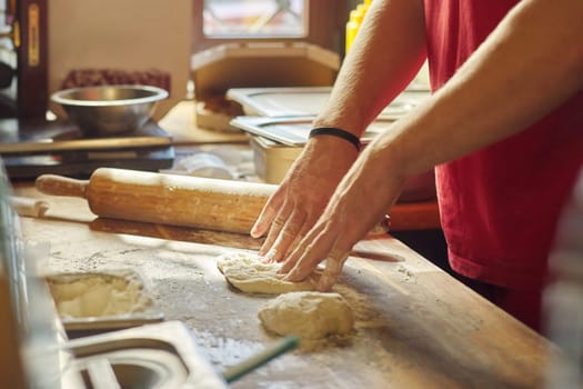 Hands of male baker with flour dough preparing food on wooden table. Cooking process, culinary, recipe