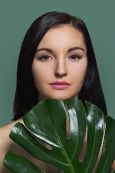 Closeup portrait of young beautiful woman with green leaf, female with natural beauty, no make-up, with extended eyelashes, green background