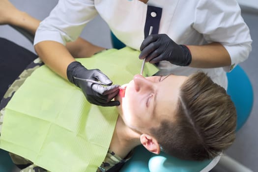 Female dentist treating teeth to patient, young man in chair at dental clinic