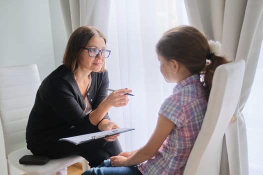 Talking girl and woman psychotherapist in office near window. Child psychology, mental health