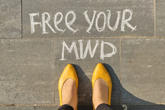 Free your mind text on gray sidewalk with woman legs, top view.