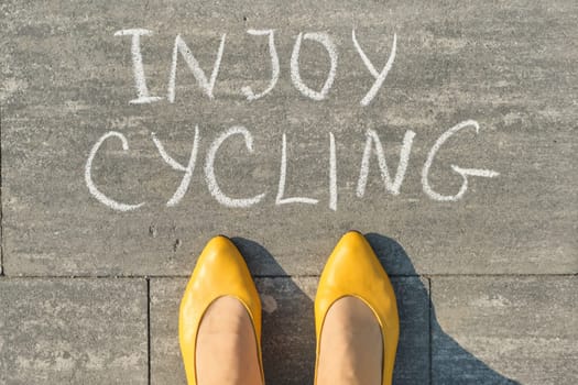 Enjoy cycling, text on gray sidewalk with woman legs, top view.