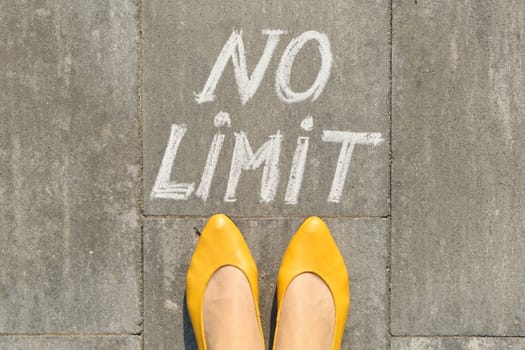 No limit text on gray sidewalk with woman legs, top view.