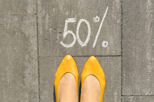 Text 50 percent written on gray pavement with woman legs, view from above.