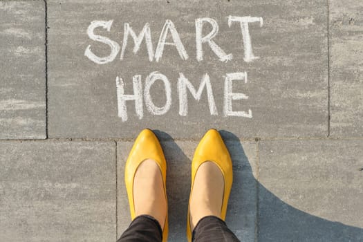 View from above, female feet with text smart home written on grey sidewalk.