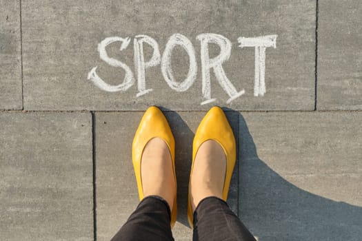 Word sport written on gray pavement with woman legs, view from above.