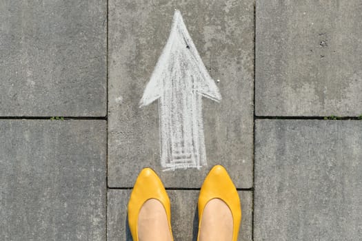 Arrow sign painted on gray sidewalk with womens legs, top view.