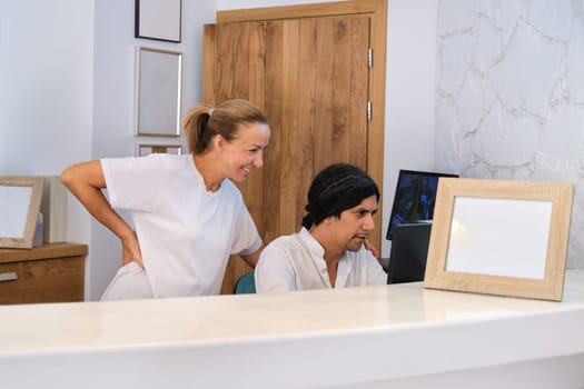 Working man and woman receptionists near reception desk, administrators looking at computer screen, bright interior of resort hotel background