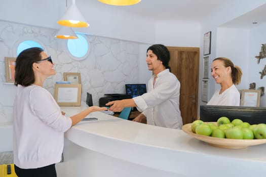 Resort hotel reception and registration of guests. Man and woman receptionists at the workplace. Guest checking in at the front desk