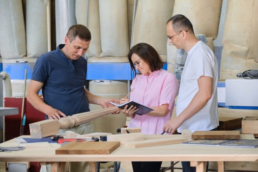 Group of working people discussing work process, wood products in carpentry workshop.