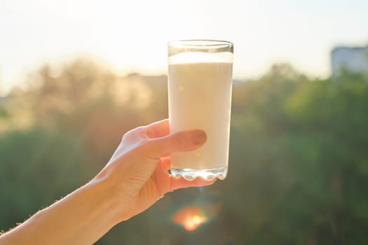 Glass with milk in womans hand, background sunset, evening city