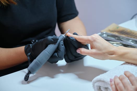 Woman doing manicure in the salon for care of hands and nails. Close up of manicure by professional electric tools
