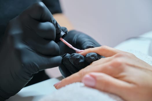 Manicurist varnishes gel nails. Professional hand and nail care in beauty salon.