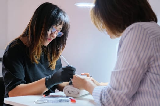 Manicurist painting nails to female client. Master beautician painting art design on nails. Professional hand and nail care in beauty salon