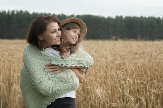 Mother hugging her little daughter, yellow ripe wheat field nature background, sunset golden hour