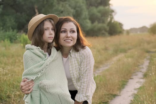 Beautiful mother hugging her little daughter, talking, smiling. Happy loving family, summer nature background golden hour, copy space