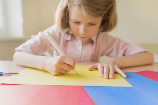 Little girl student studying sitting at her desk, schoolgirl drawing writing in pen on colored paper. School, education, knowledge and children