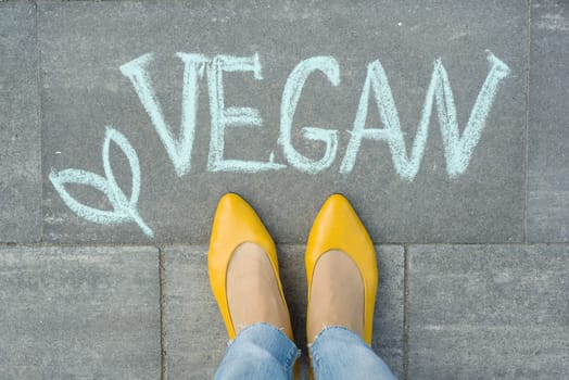 Female feet with text vegan written on grey sidewalk.