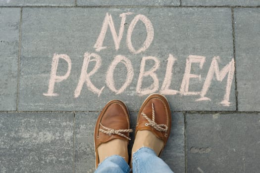 Female feet with text no problem written on grey sidewalk.