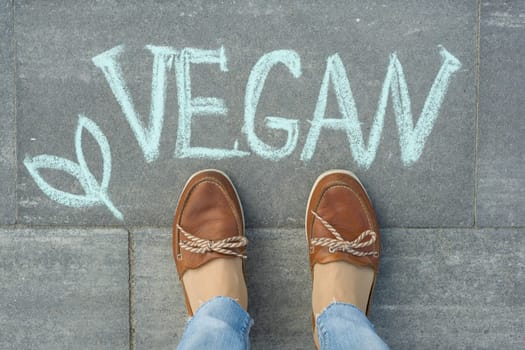 Female feet with text vegan written on grey sidewalk.