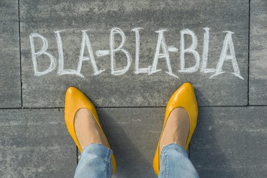 Female feet with text bla-bla-bla written on grey sidewalk.