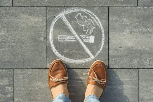 Female feet with picture no smoking painted on the grey sidewalk.