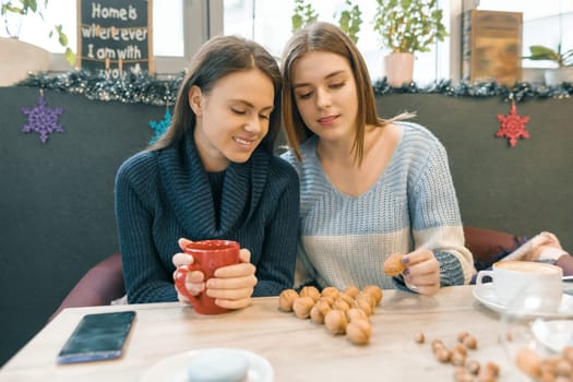 Winter Christmas holidays, young women in cafe drink hot drinks, lay on the table walnuts in shape of Christmas tree