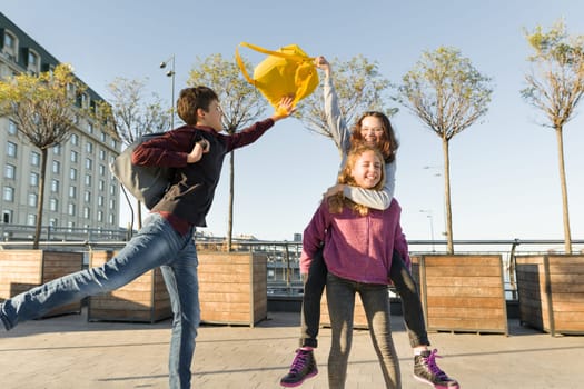 Friends teenagers students with school backpacks, having fun on the way from school. City background, golden hour