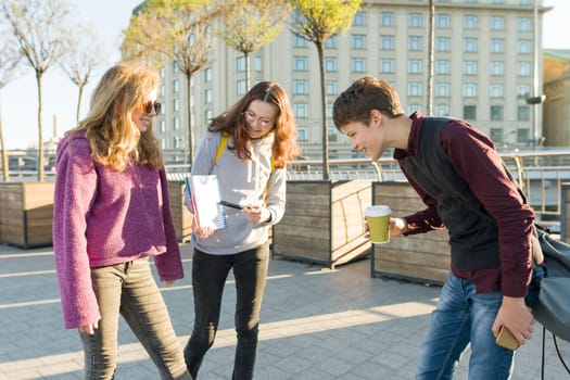 High school students are talking outdoor. Girl teenager showing on a clean white sheet in notebook and boy looking at notebook, the golden hour